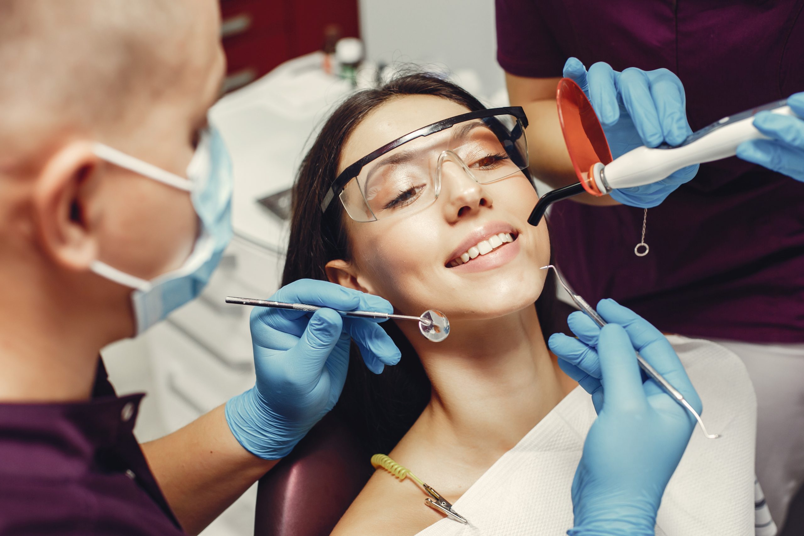 The dentist treats the girl's teeth. A young woman visited a dentist. The doctor works with an assistant
